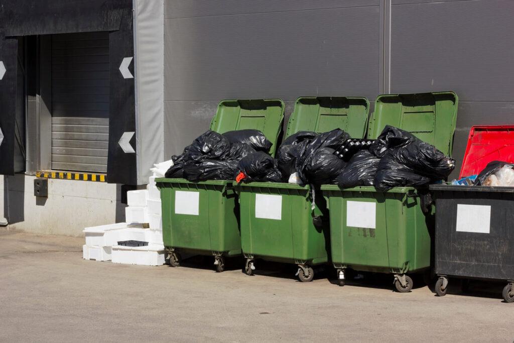 Überfüllte Mülltonnen in einem industriellen Bereich, die einen effektiven Mülltonnen Sichtschutz benötigen, um Ordnung und Sauberkeit zu gewährleisten