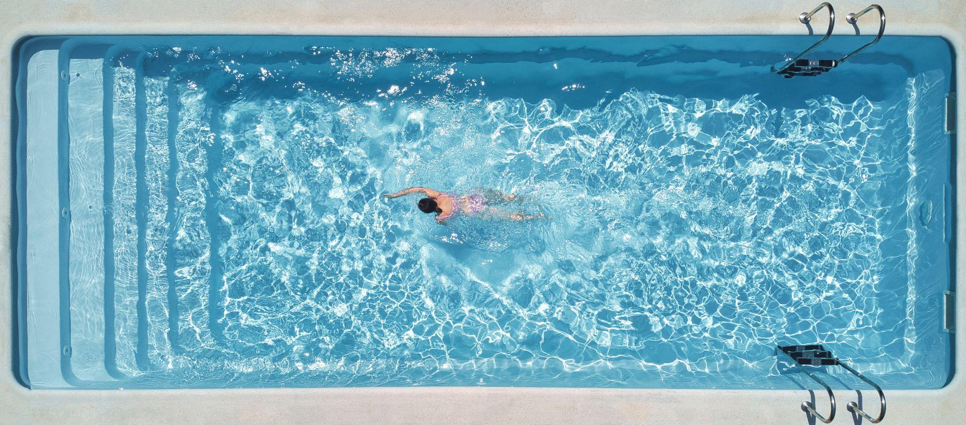 Frau schwimmt in einem modernen rechteckigen Pool mit klarer Wasseroberfläche.