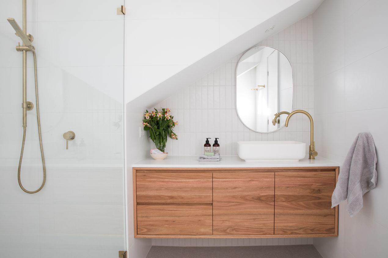 Kompaktes Badezimmer unter Dachschräge mit Holz-Waschtisch, heller Duschrückwand und goldenen Armaturen